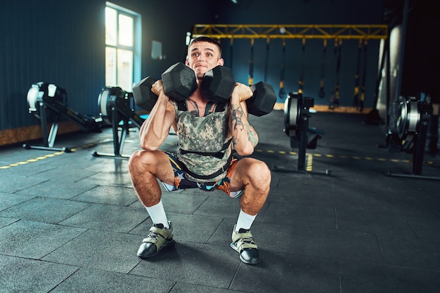 Homem jovem e bonito atleta fazendo exercícios para os músculos das mãos de halteres no ginásio. Crossfit e conceito de saúde