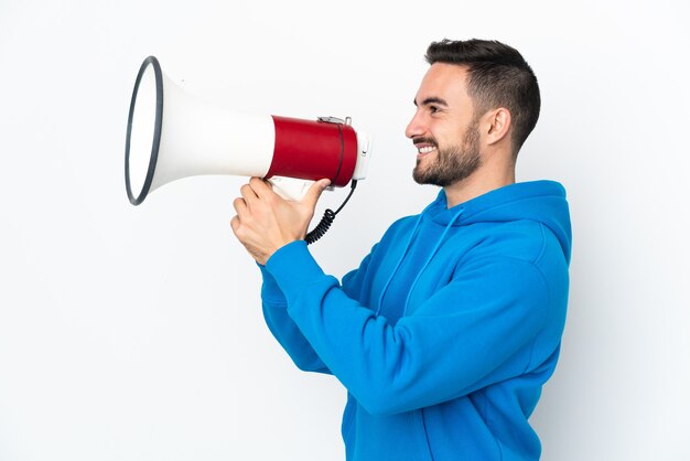 Homem jovem e bonito, caucasiano, isolado no fundo branco, gritando em um megafone para anunciar algo