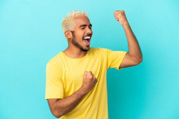 Foto homem jovem e bonito colombiano isolado em um fundo azul comemorando uma vitória