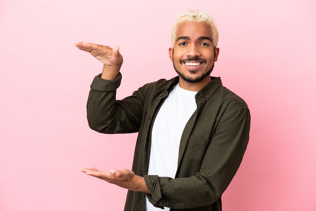 Homem jovem e bonito colombiano isolado em um fundo rosa segurando copyspace para inserir um anúncio