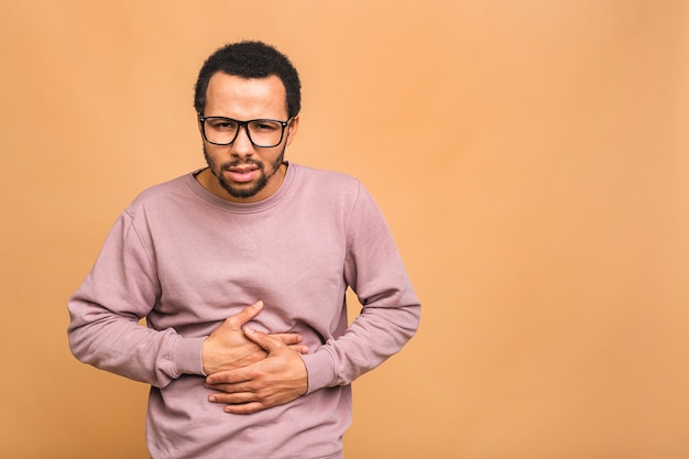 Homem jovem e bonito com a mão na barriga por causa de indigestão, doença dolorosa, mal-estar