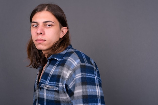 Foto homem jovem e bonito hippie andrógino com cabelo comprido contra uma parede cinza