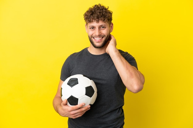 Homem jovem e bonito jogador de futebol isolado em um fundo amarelo rindo