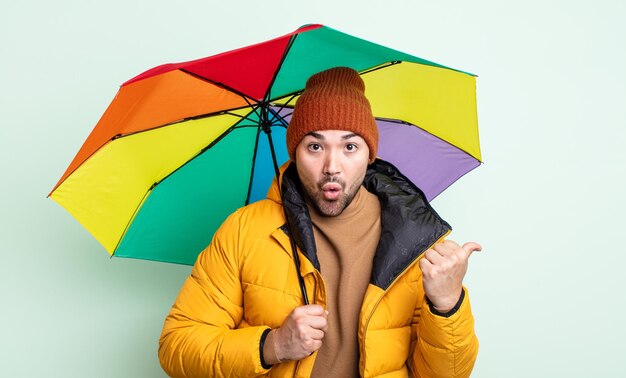 Homem jovem e bonito parecendo espantado com a descrença. conceito de chuva e guarda-chuva