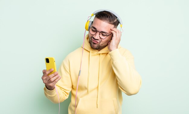 Homem jovem e bonito se sentindo entediado, frustrado e com sono depois de um cansativo. conceito de fones de ouvido e smartphone