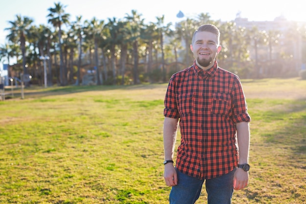 Homem jovem e bonito sorridente em pé na grama no parque. Verão no conceito de cidade.