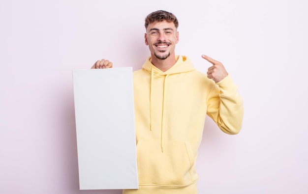 Homem jovem e bonito sorrindo com confiança, apontando para o próprio sorriso largo. conceito de tela em branco