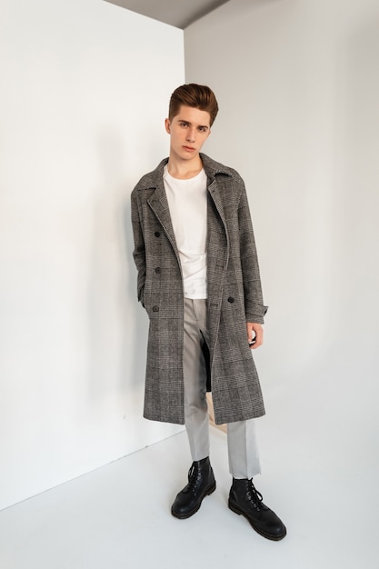 Homem jovem e elegante elegante em roupas da moda casuais com casaco em estúdio