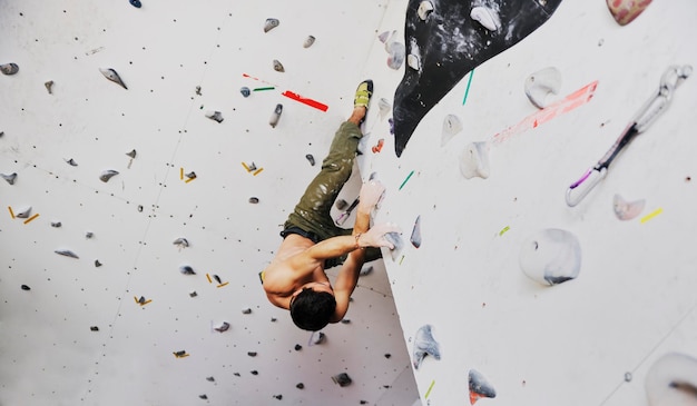 homem jovem e em forma exercita alpinismo livre na parede de prática interna