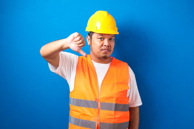 Homem jovem e gordo trabalhador da construção civil asiático com capacete e colete laranja e parece infeliz