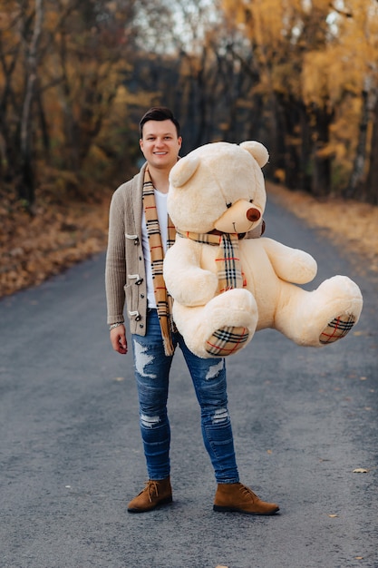 Foto homem jovem, em, outono, parque, estrada, com, grande, urso, brinquedo