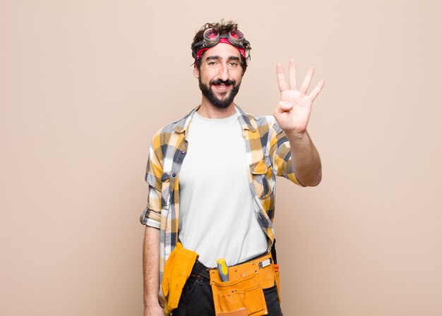 Homem jovem empregada sorrindo e olhando amigável, mostrando o número quatro ou quarto com a mão para a frente, contando contra a parede plana