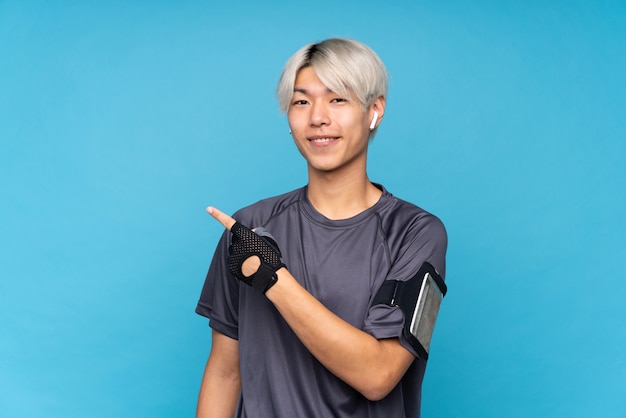 Homem jovem esporte asiático sobre azul isolado apontando para o lado para apresentar um produto