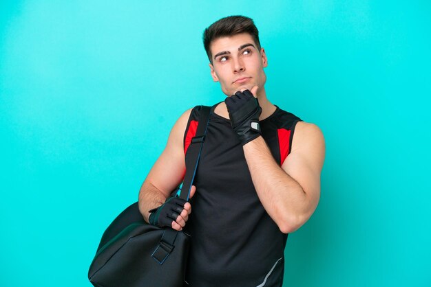 Homem jovem esporte caucasiano com bolsa esportiva isolada em fundo azul e olhando para cima