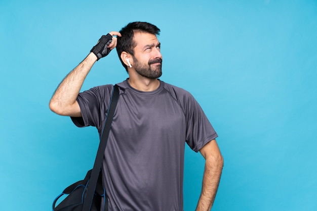 Homem jovem esporte com barba sobre parede azul isolada, tendo dúvidas ao coçar a cabeça