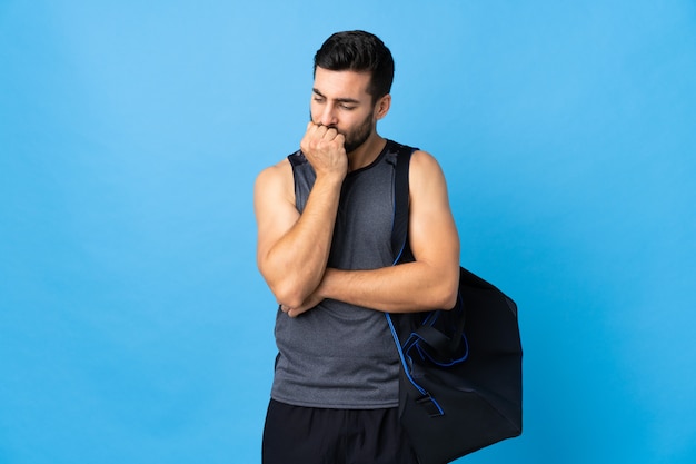Foto homem jovem esporte com saco de esporte isolado na parede azul, tendo dúvidas