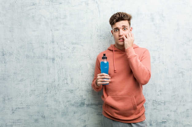 Homem jovem esporte segurando uma bebida energética, roer unhas, nervosas e muito ansiosas.