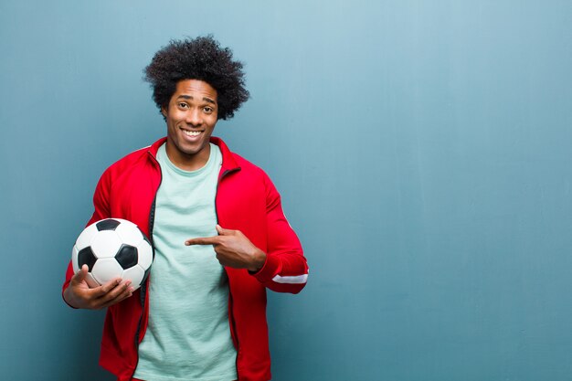 Homem jovem esportes preto com uma bola de futebol contra a parede azul grunge