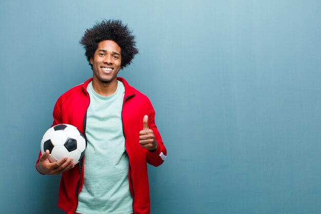 Homem jovem esportes preto com uma bola de futebol contra wa grunge azul