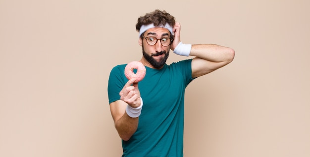 Homem jovem esportes tendo um lanche segurando um donut de açúcar rosa