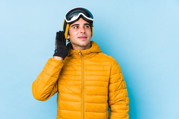 Homem jovem esquiador usando óculos de snowboard isolados, tentando ouvir uma fofoca.