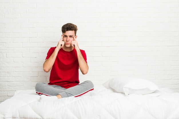 Foto homem jovem estudante adolescente na cama focado em uma tarefa, mantendo os indicadores apontando a cabeça.