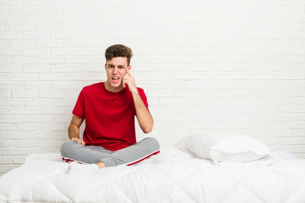 Homem jovem estudante adolescente na cama mostrando um gesto de decepção com o dedo indicador.