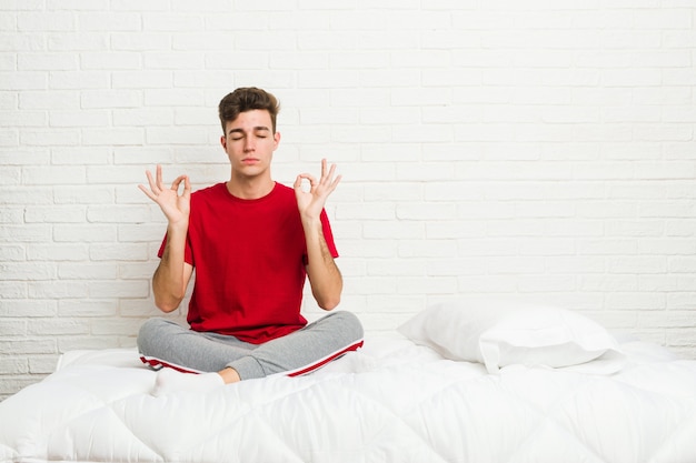 Homem jovem estudante adolescente na cama relaxa após um duro dia de trabalho, ela está realizando ioga.