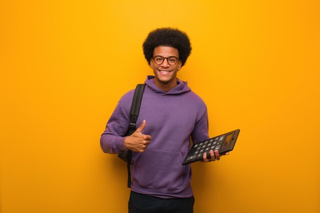 Homem jovem estudante afro-americano segurando uma calculadora sorrindo e levantando o polegar