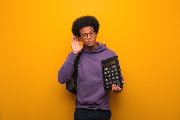 Homem jovem estudante afro-americano, segurando uma calculadora tentar ouvir uma fofoca