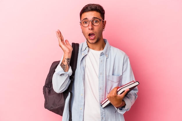 Homem jovem estudante caucasiano segurando livros isolados no fundo rosa surpreso e chocado.