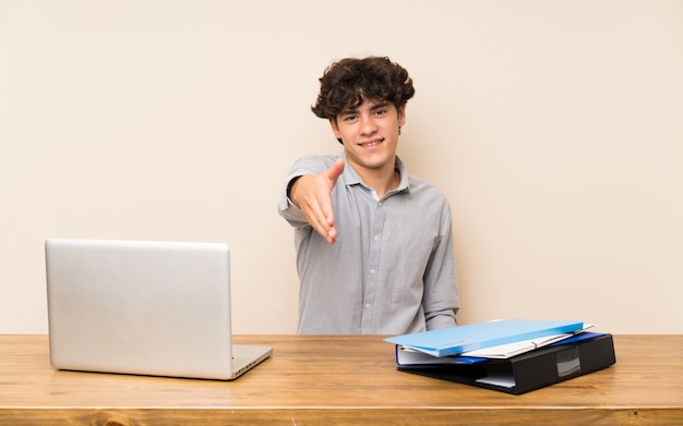 Homem jovem estudante com um laptop apertando as mãos para fechar um bom negócio