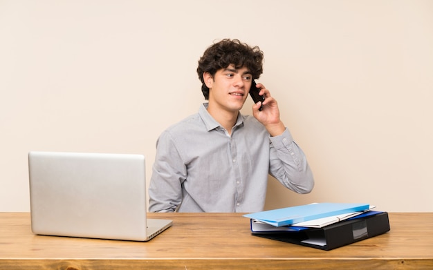 Homem jovem estudante com um laptop, mantendo uma conversa com o telefone móvel