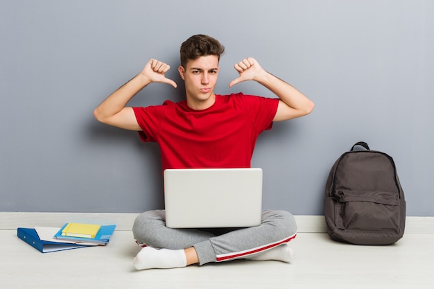 Homem jovem estudante sentado no chão de sua casa segurando um laptop