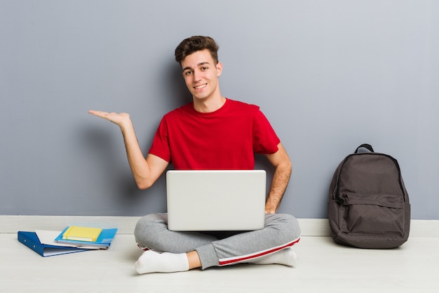 Homem jovem estudante sentado no chão de sua casa segurando um laptop