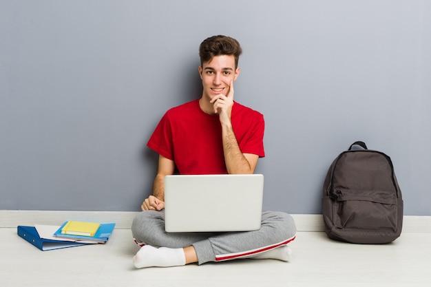 Homem jovem estudante sentado no chão de sua casa segurando um laptop