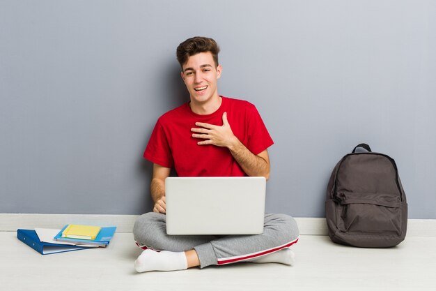 Homem jovem estudante sentado no chão de sua casa segurando um laptop