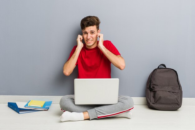 Homem jovem estudante sentado no chão de sua casa segurando um laptop