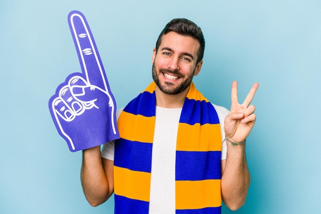 Homem jovem fã de esportes isolado em fundo azul, mostrando o número dois com os dedos