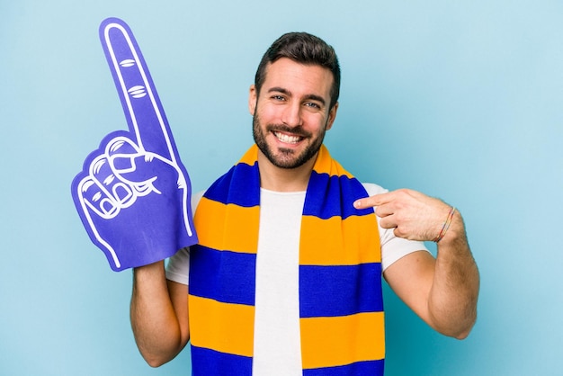 Homem jovem fã de esportes isolado na pessoa de fundo azul apontando com a mão para um espaço de cópia de camisa orgulhoso e confiante