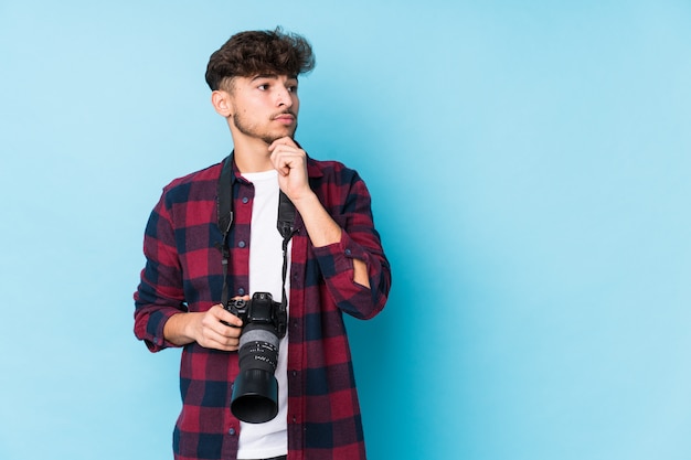 Homem jovem fotógrafo árabe olhando de soslaio com expressão duvidosa e cética.