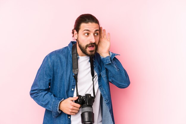 Homem jovem fotógrafo caucasiano isolado tentando ouvir uma fofoca.