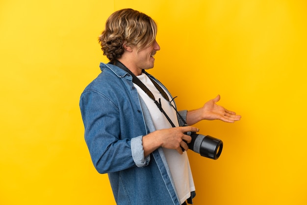 Homem jovem fotógrafo isolado em um fundo amarelo com expressão de surpresa enquanto olha de lado