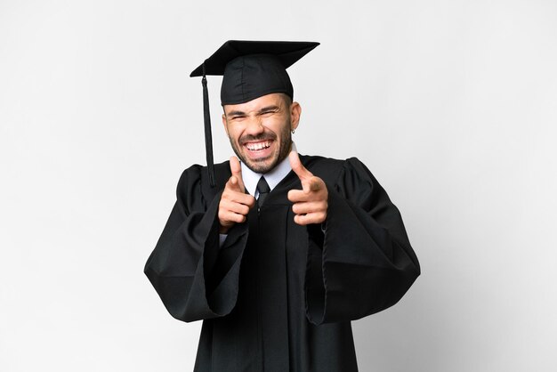 Homem jovem graduado da universidade sobre fundo branco isolado, apontando para a frente e sorrindo