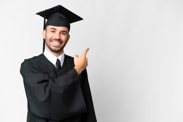 Homem jovem graduado da universidade sobre fundo branco isolado, apontando para trás