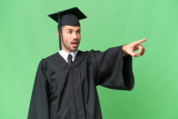 Homem jovem graduado da universidade sobre fundo isolado, apontando para fora