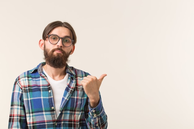 Homem jovem hippie apontando para uma parede branca com espaço de cópia