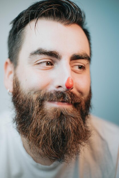 Homem jovem hippie com barba e tinta vermelha no nariz sorrindo e jogando retrato, conceito jovem artista, retrato de perto, imagem engraçada, criatividade e diversão