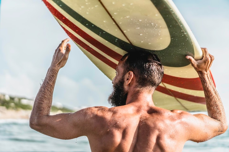 Foto homem jovem hippie com prancha de surf na cabeça cumprimentando amigos com um gesto cara se divertindo fazendo esporte radical homem barbudo desportivo treinando com prancha de surf no mar conceito de liberdade de estilo de vida