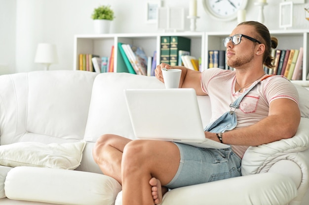 Homem jovem hippie em casa, relaxando, tomando café